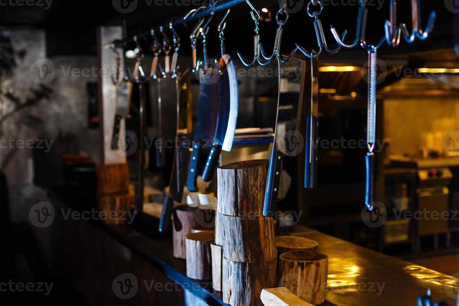 muitas facas grandes penduradas em armazenamento de madeira na cozinha do restaurante foto