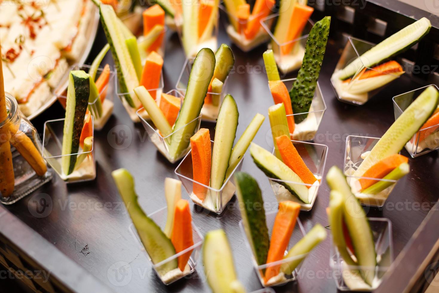 catering para festa. close-up de aperitivos com tomate cereja, azeitonas verdes, azeite, queijo e especiarias em copos curtos na mesa de madeira marrom. foto