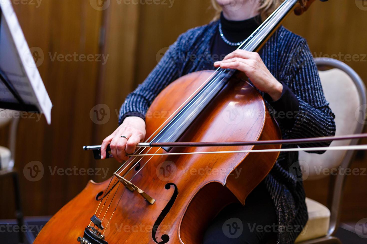 uma jovem toca violoncelo no escuro. mãos no violoncelo foto