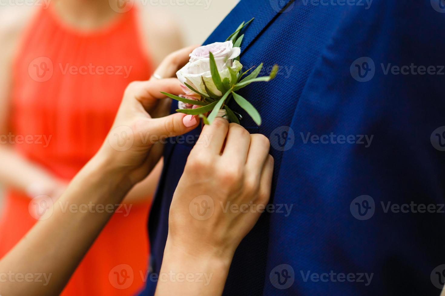 feche as mãos da noiva prendendo a lapela na jaqueta do noivo foto