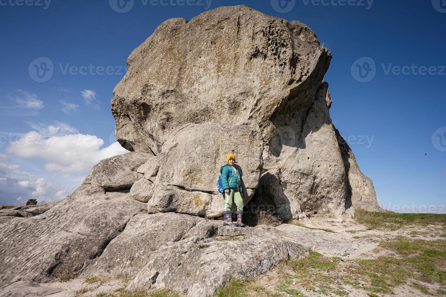 explorando a natureza. menino usa mochila caminhando perto de pedra grande na colina. pidkamin, ucrânia. foto