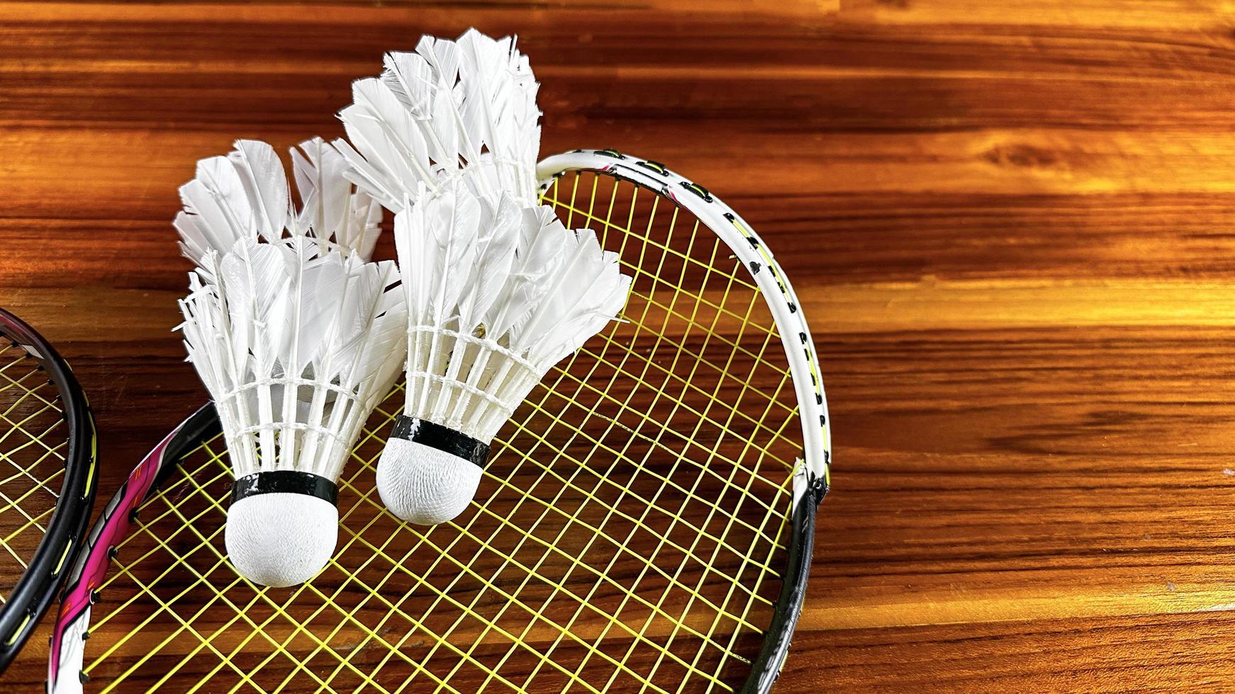 close-up de raquetes de badminton quebradas e galos de peteca de badminton branco sobre fundo de madeira marrom foto