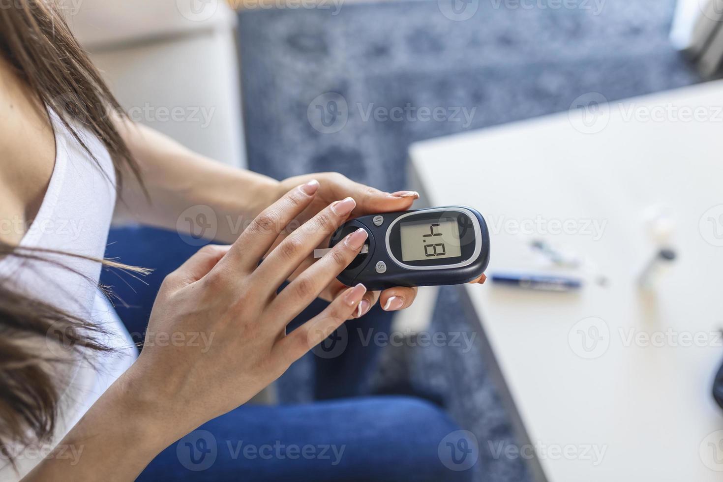 jovem mulher usando glicosímetro digital em casa. controle de diabetes foto