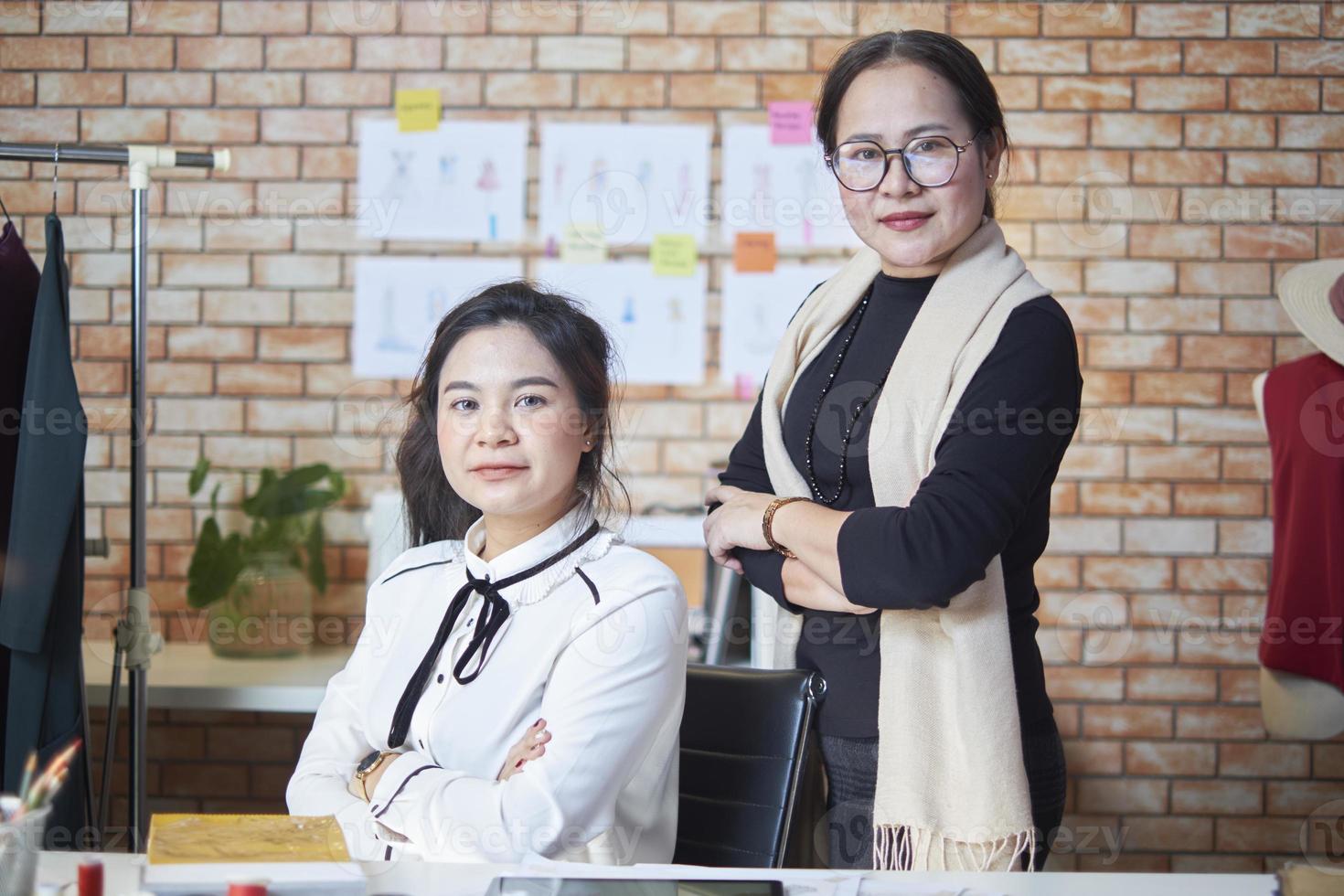 equipe de moda, estilista asiática madura e assistente adolescente tailandesa no estúdio de design de roupas, braços cruzados e sorriso, trabalhos de costura felizes para design de vestidos, empresário de alfaiataria profissional. foto