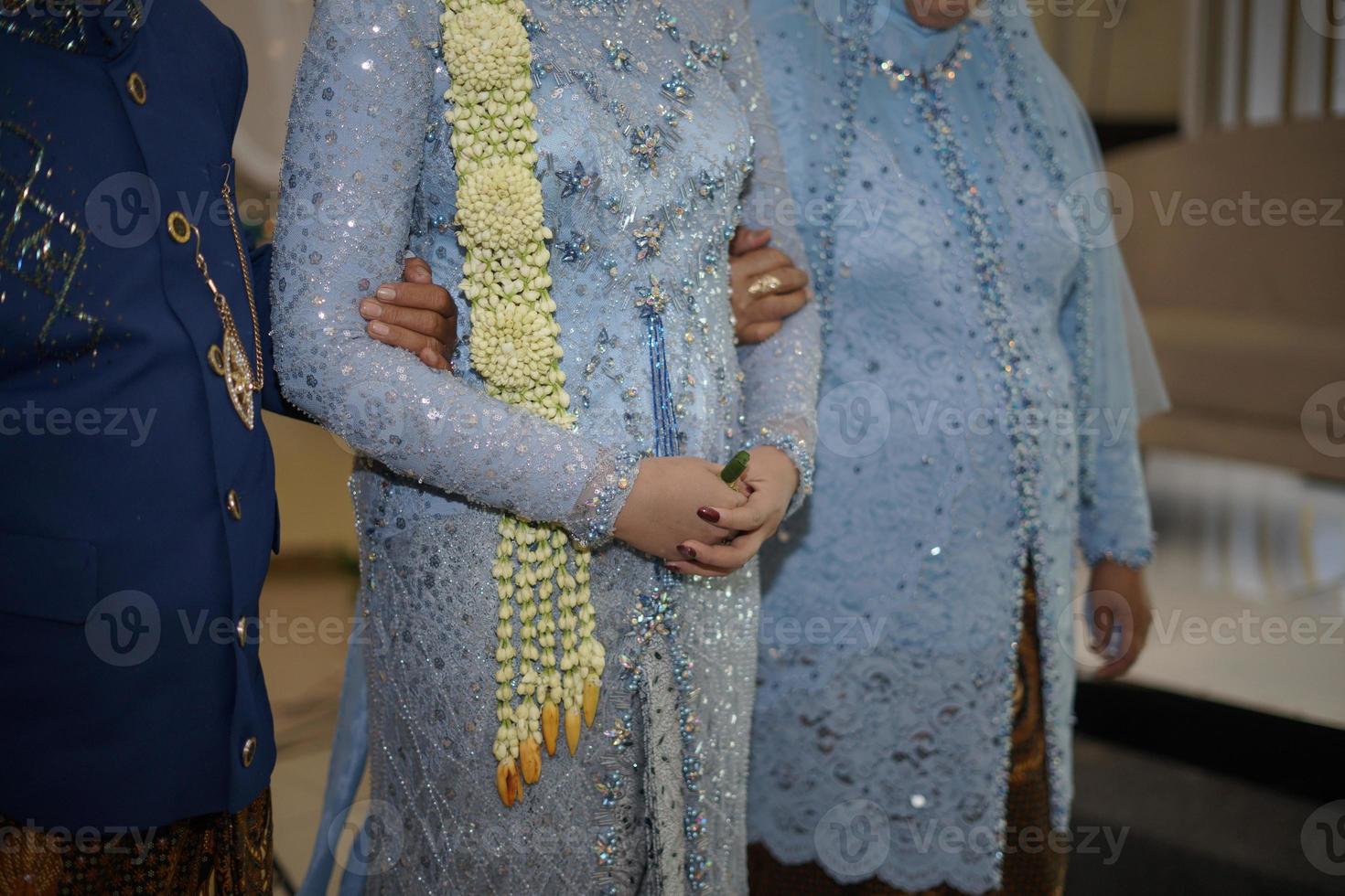 pais segurando sua linda noiva usando vestido de noiva com colar de flores de jasmim e magnólia para uma cerimônia de casamento tradicional na indonésia foto