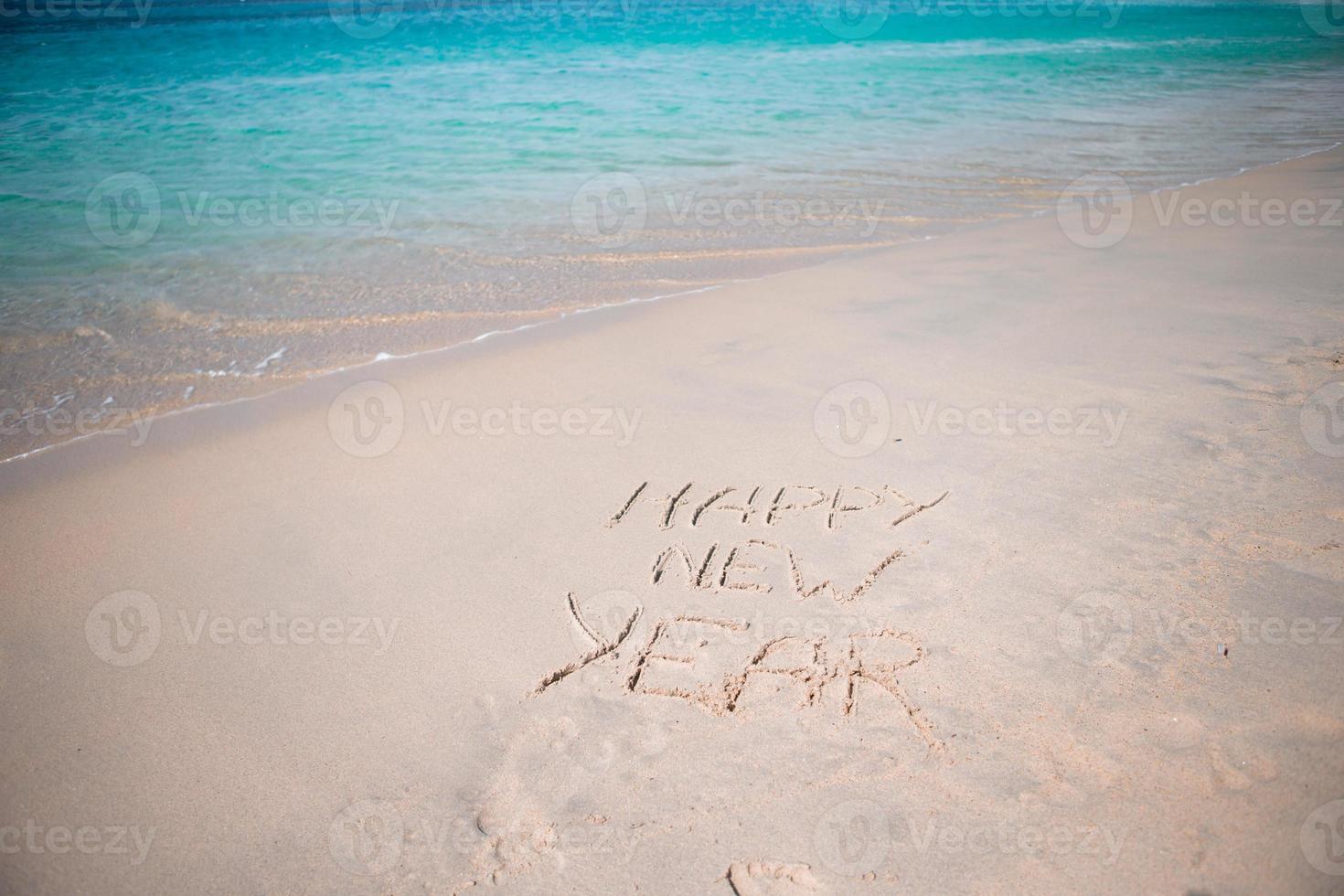 feliz ano novo escrito na areia branca foto