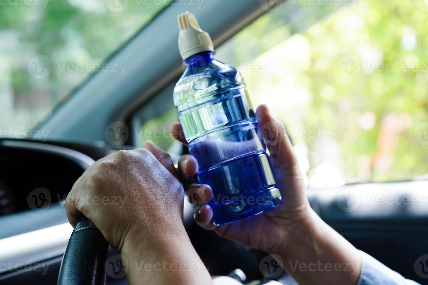 motorista de mulher asiática segura água fria para beber no carro, perigoso e arrisca um acidente. foto