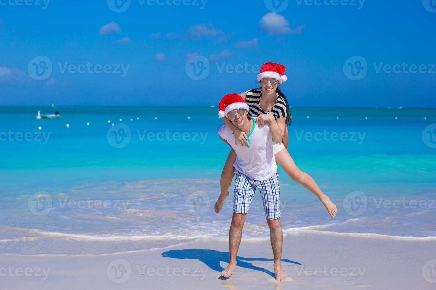 jovem casal feliz em chapéus de papai noel vermelhos durante suas férias tropicais foto