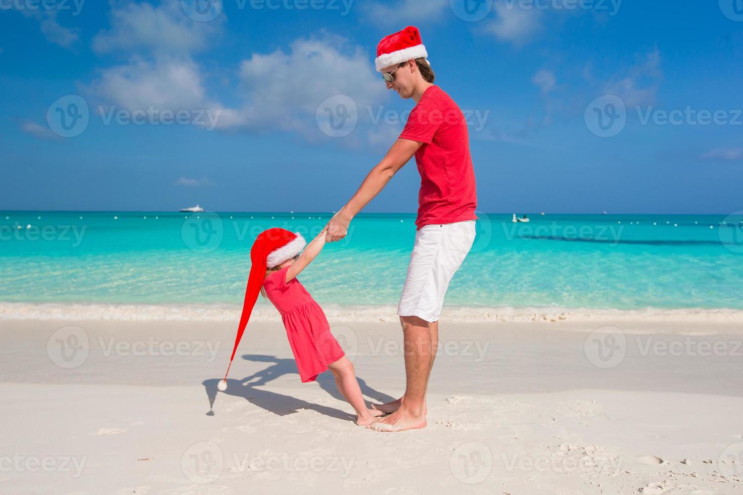 menina e pai feliz com chapéu de Papai Noel se divertem na praia tropical foto