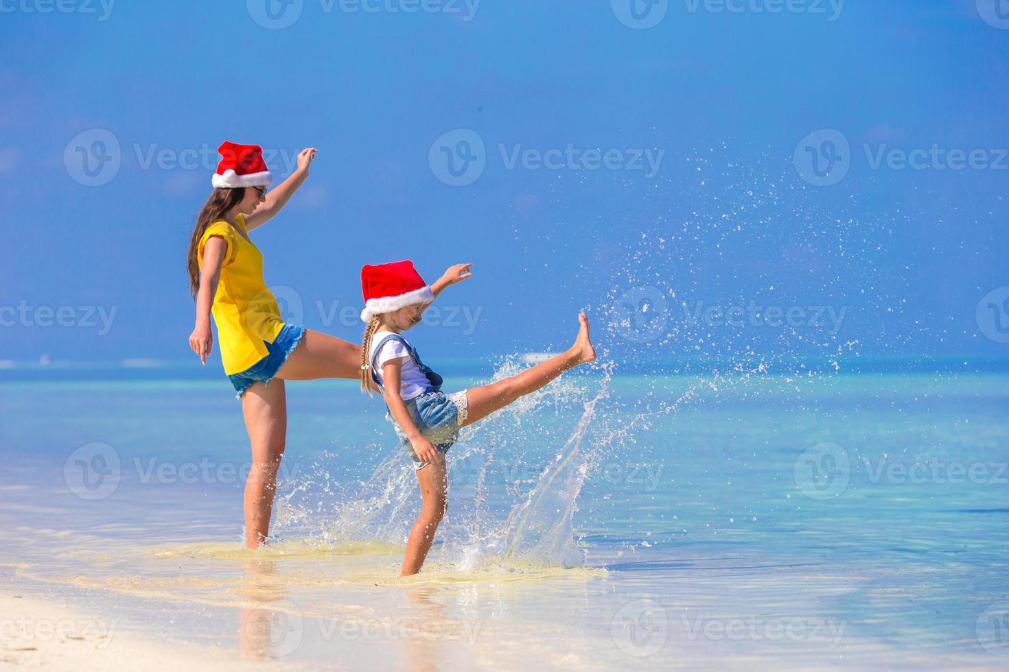 menina e jovem mãe com chapéu de Papai Noel durante as férias na praia foto