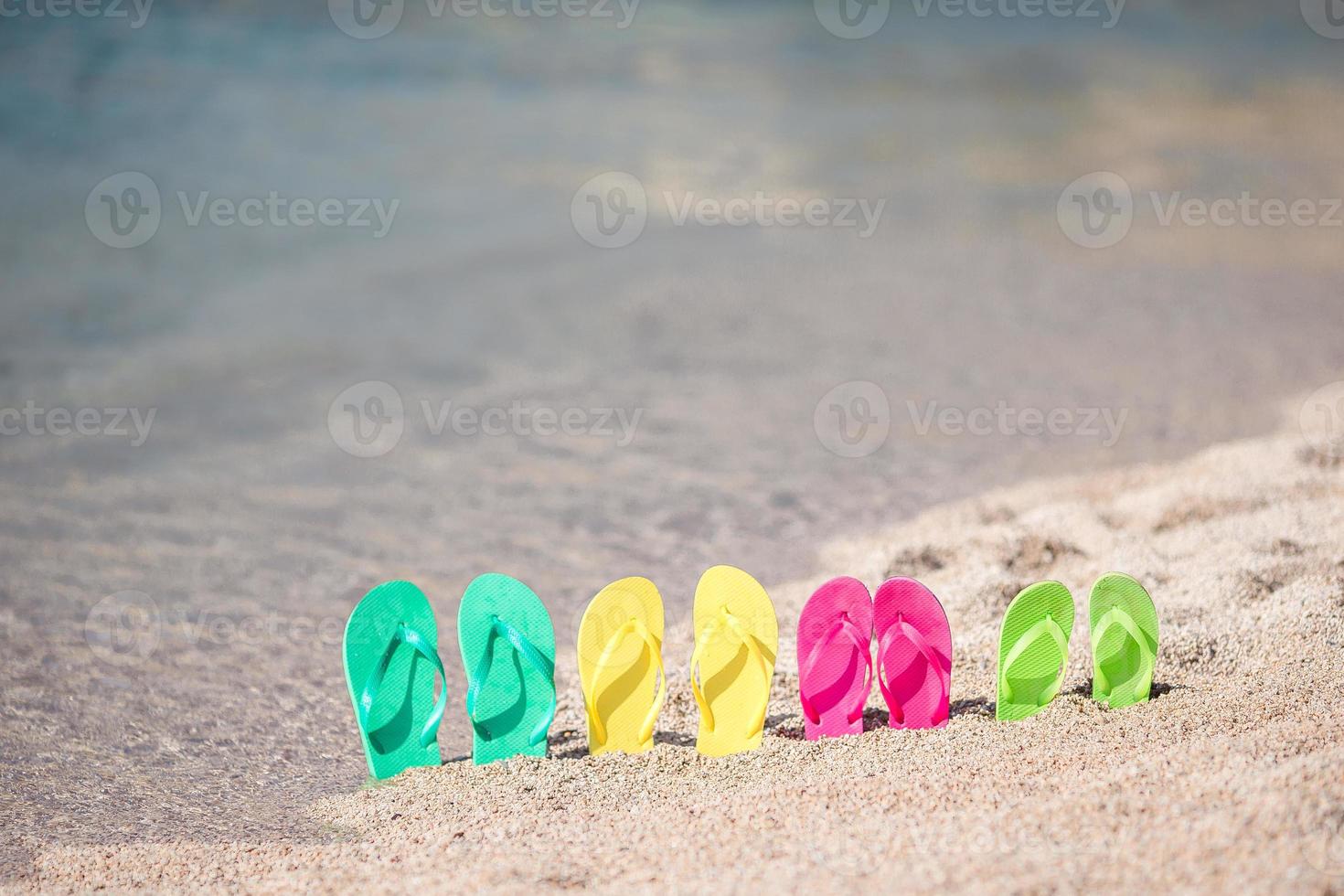 chinelos coloridos da família na praia em frente ao mar foto