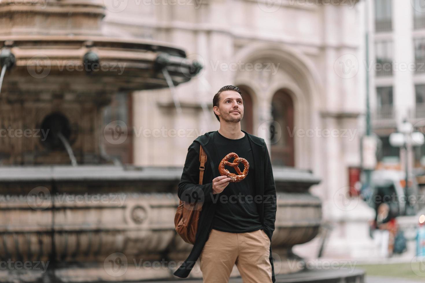 belo jovem segurando pretzel e relaxando no parque foto