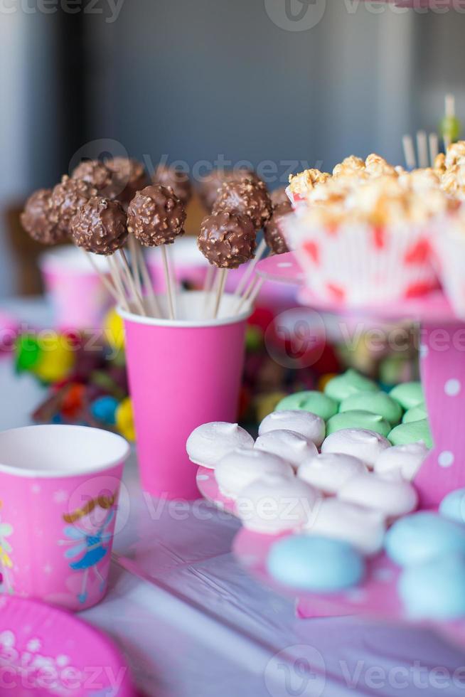 merengues coloridos doces, pipoca, bolos de nata e bolos pops na mesa foto