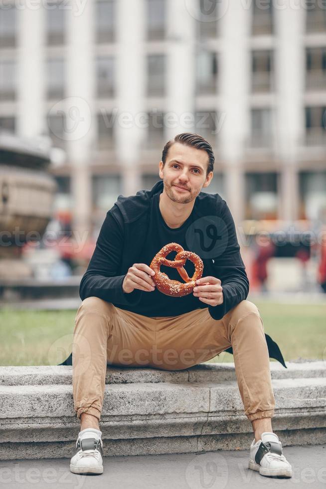 belo jovem segurando pretzel e relaxando no parque foto