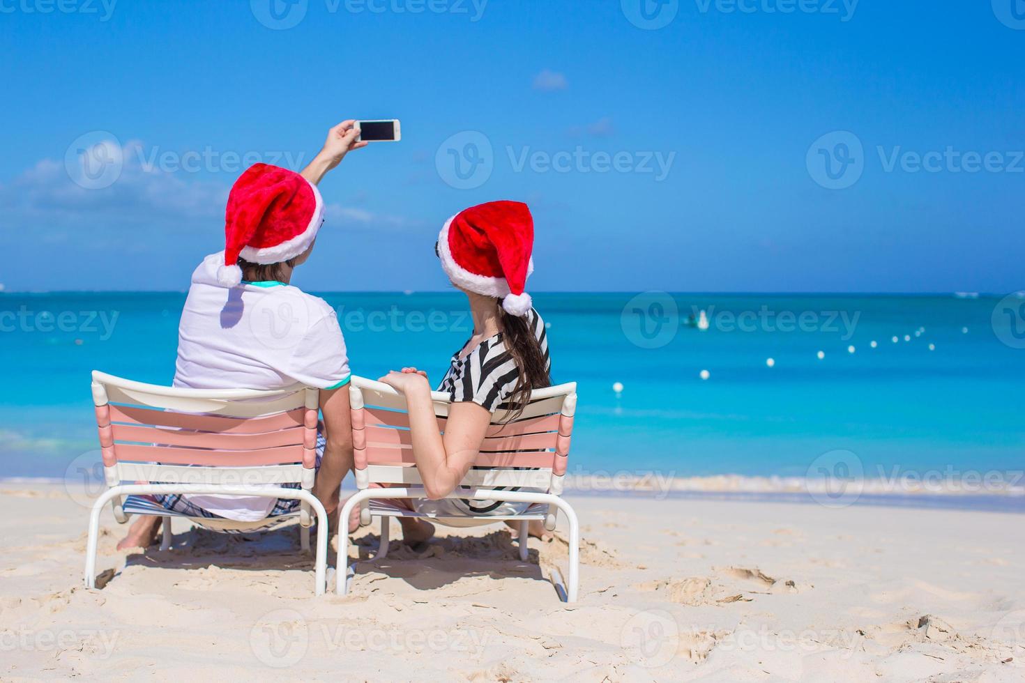 casal feliz usando chapéu de Papai Noel na praia do Caribe foto