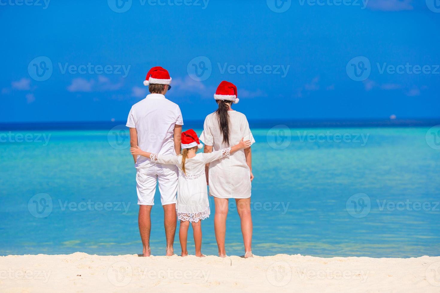 família feliz de três em chapéus de papai noel durante as férias tropicais foto