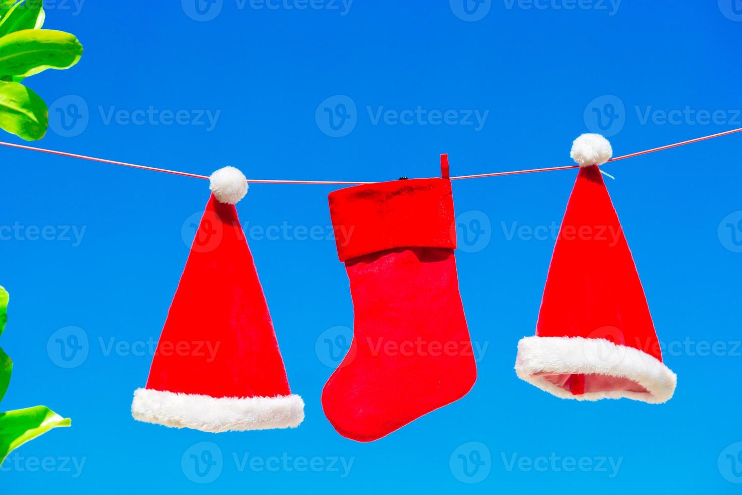 chapéus de papai noel vermelhos e meia de natal entre palmeiras na praia branca foto