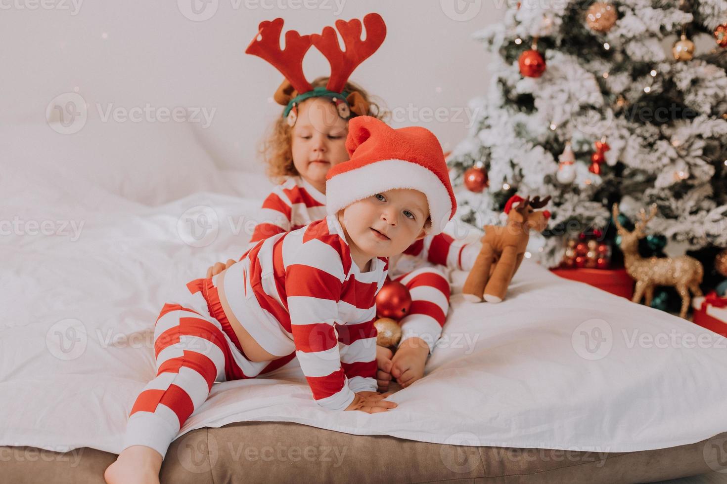 crianças de pijama vermelho e branco comem doces de natal sentados na cama. irmão e irmã, menino e menina compartilham presentes. manha de Natal. estilo de vida. espaço para texto. foto de alta qualidade