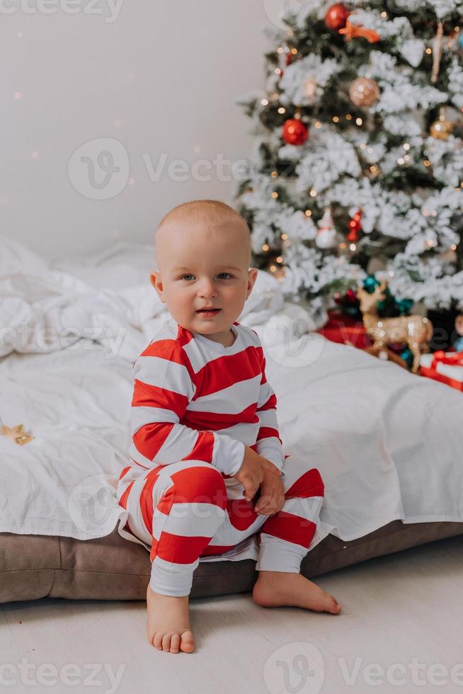 garotinho de pijama vermelho e branco come um lindo biscoito caseiro de natal sentado na cama com um cachorro. criança e animal de estimação. estilo de vida. foto de alta qualidade