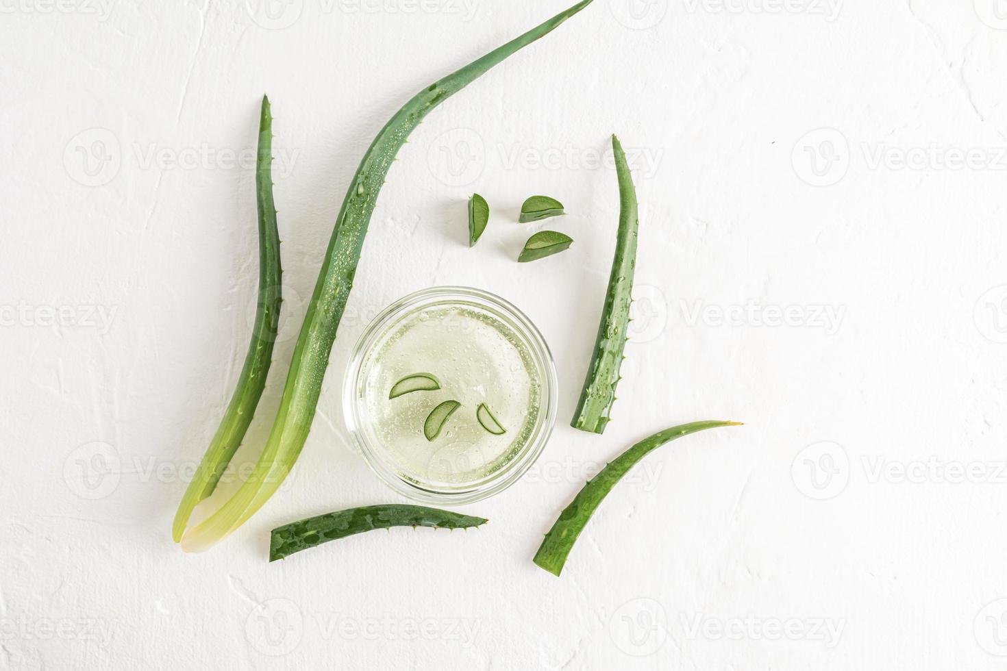 gel de aloe vera natural em uma tigela de vidro em um fundo branco com pedaços de aloe fresco e folhas verdes da planta. disposição plana. cosméticos naturais. foto