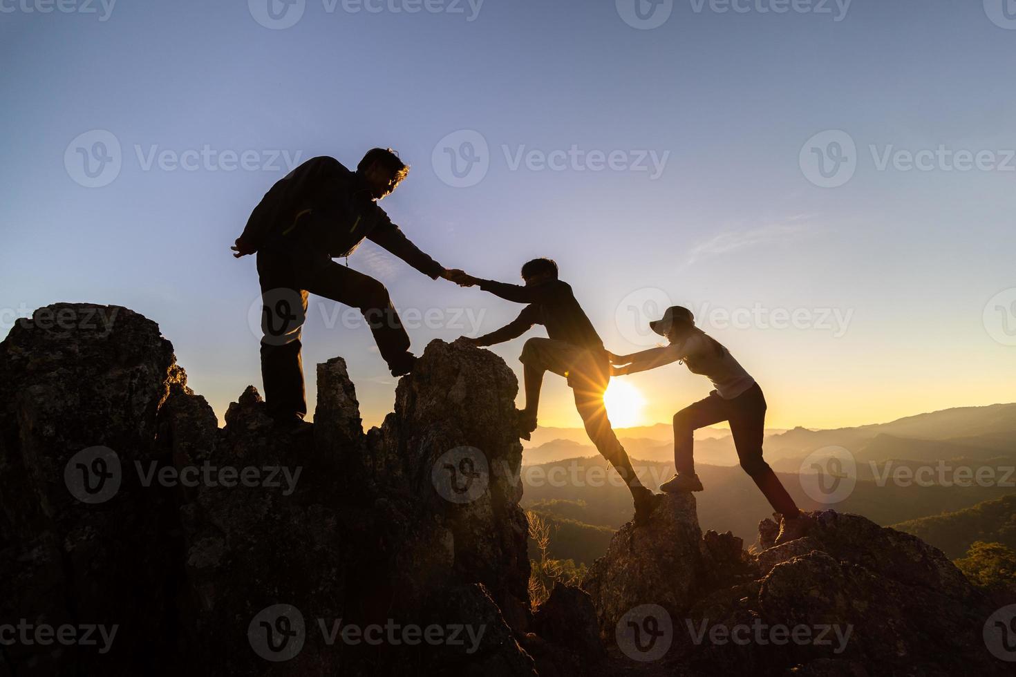 silhueta do trabalho em equipe de três alpinistas ajudando uns aos outros no topo da equipe de alpinismo. caminhadas de amizade de trabalho em equipe ajudam uns aos outros silhueta de assistência de confiança nas montanhas, nascer do sol. foto