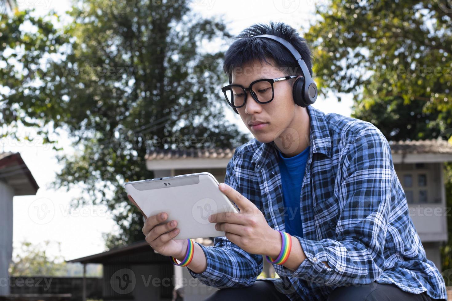 retrato jovem asiático usa pulseira de arco-íris e ouve música no tablet na mão, o conceito de ser assertivo ao apresentar sua verdadeira identidade lgbt para a sociedade de hoje é aceito pela sociedade. foto