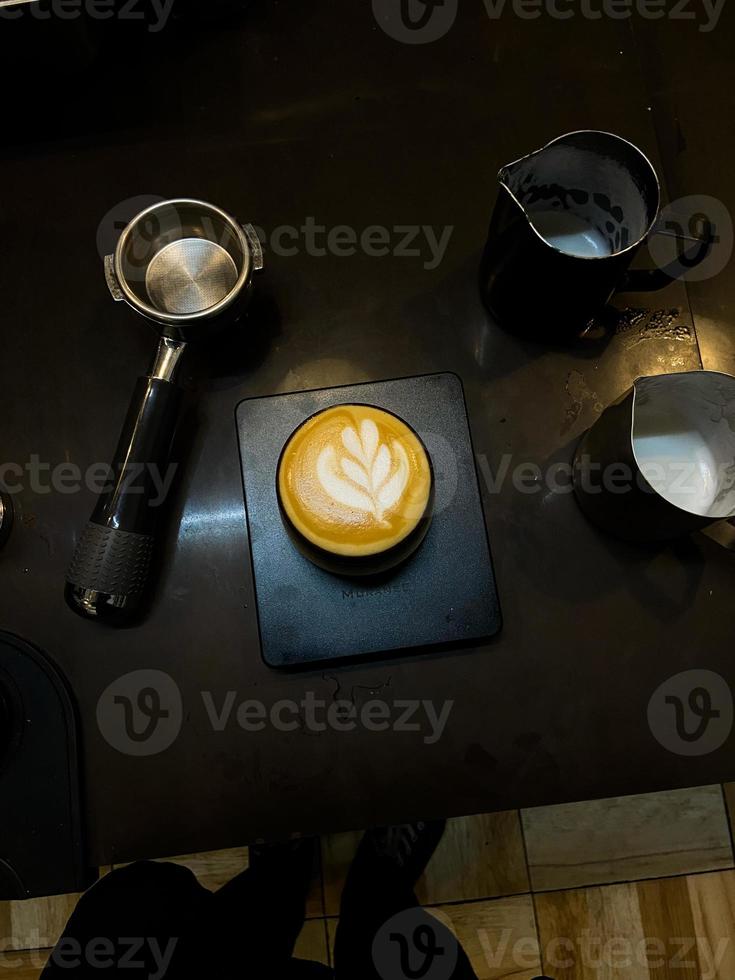 xícara de café com bela arte latte na mesa preta com ferramentas de cafeteira. bebidas no café da manhã foto