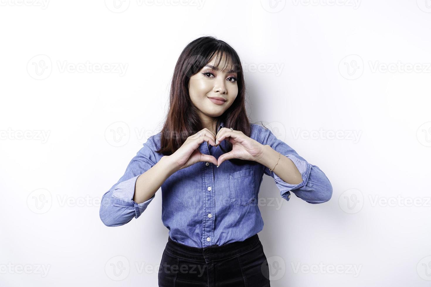 uma jovem asiática feliz vestindo uma camisa azul sente formas românticas gesto do coração expressa sentimentos ternos foto