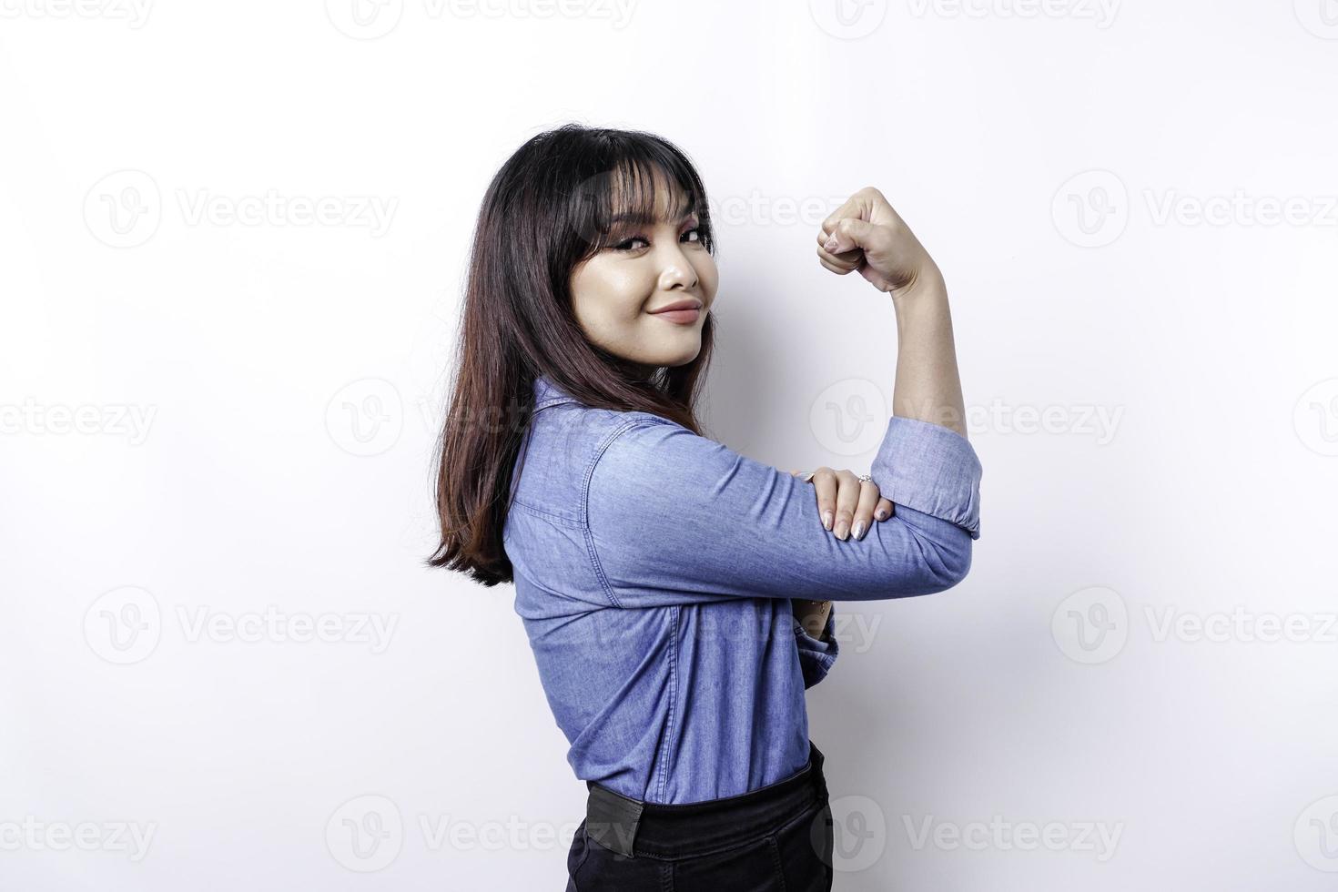 mulher asiática animada, vestindo uma camisa azul, mostrando um gesto forte, levantando os braços e os músculos sorrindo orgulhosamente foto