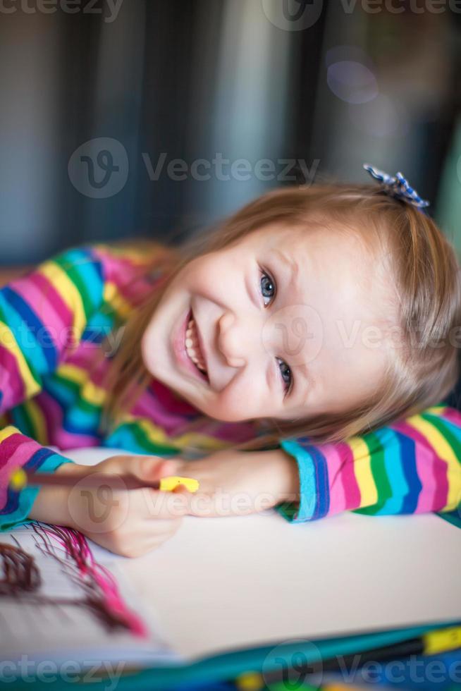 menina bonitinha pintando com lápis enquanto está sentado na mesa dela foto