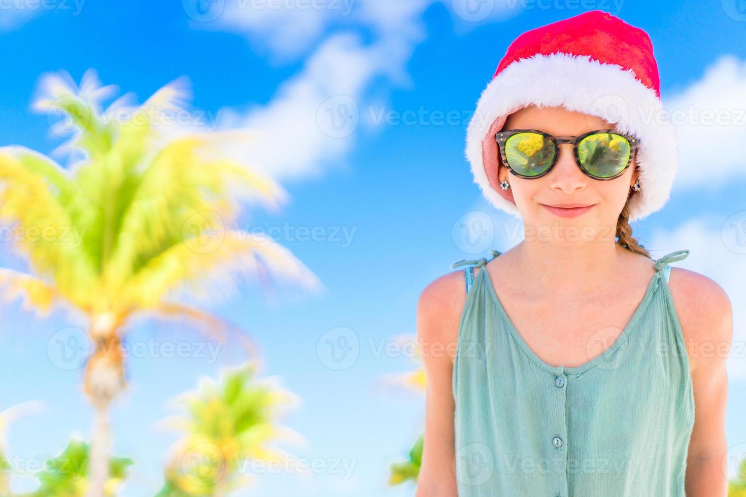 adorável menina de chapéu de Papai Noel durante as férias na praia de natal foto