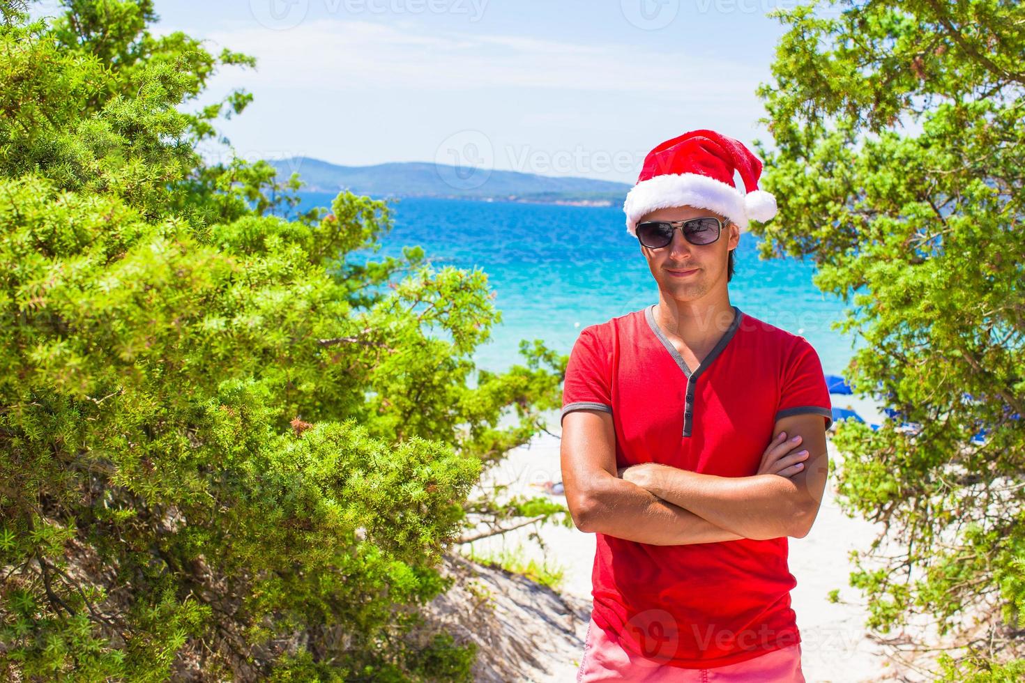 jovem de chapéu vermelho de natal na praia tropical perto dos abetos foto