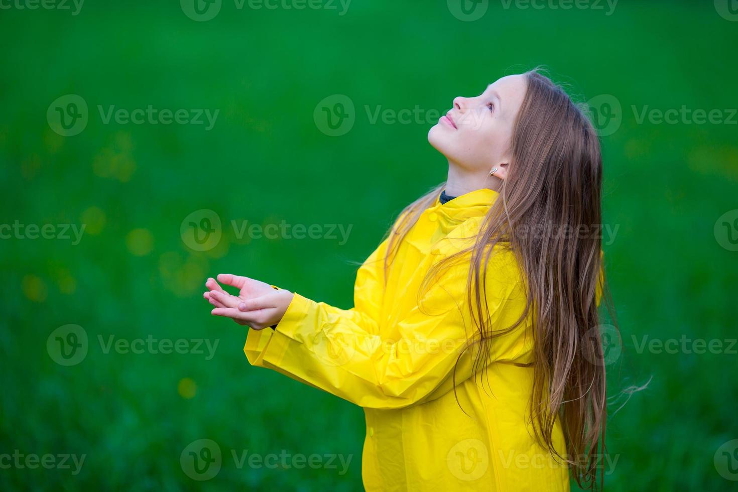 menina na capa de chuva brincando na chuva ao ar livre foto
