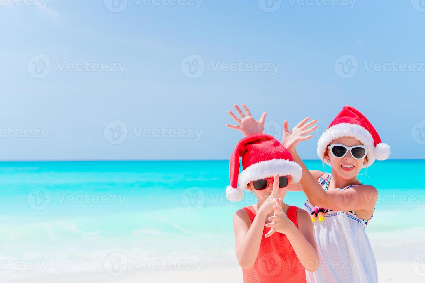 adoráveis crianças se divertem com chapéu de Papai Noel durante as férias na praia de natal. ano novo na praia foto