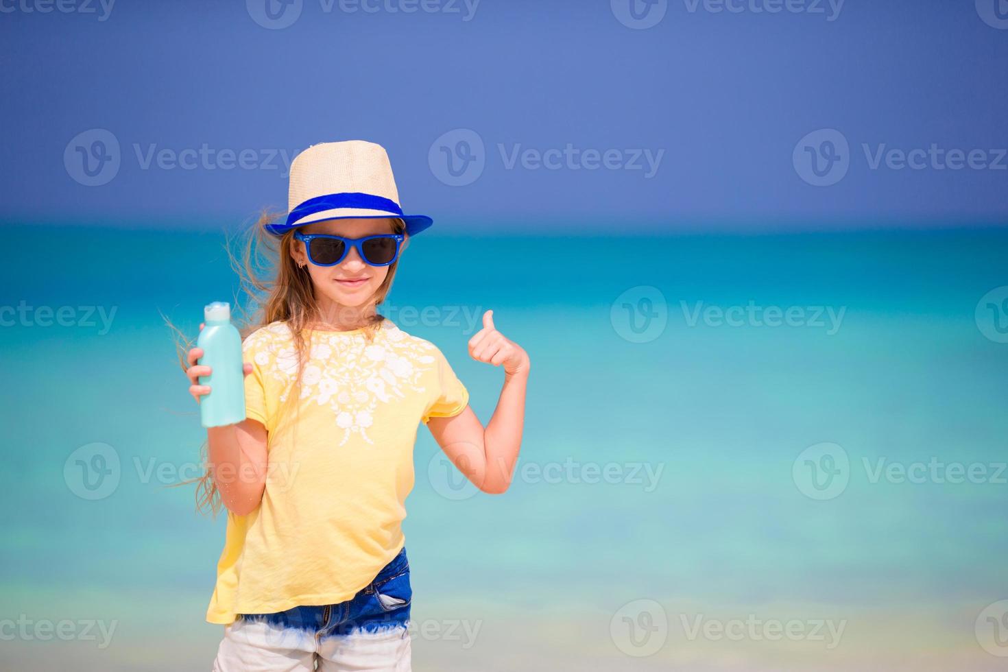 menina adorável com garrafa de protetor solar na praia foto