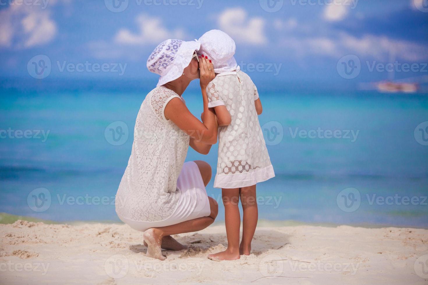 jovem mãe contando um segredo ao ouvido de sua filhinha foto