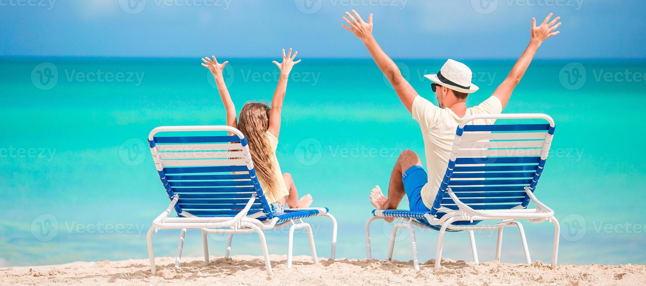 panorama da família de pai e filho mãos para cima na praia sentado na chaise-longue foto