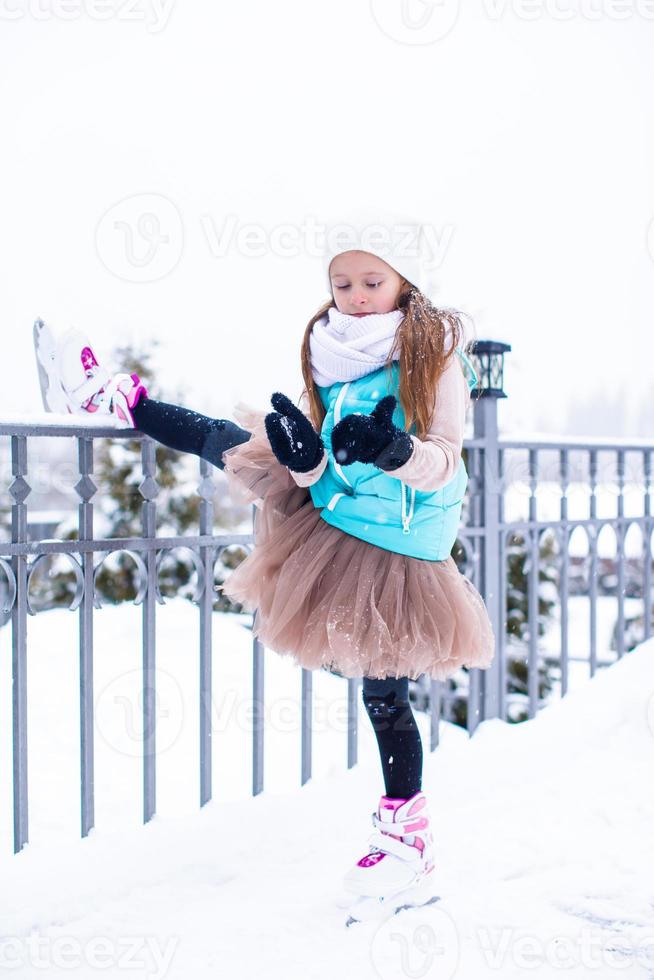 adorável menina patinando na pista de gelo ao ar livre em dia de neve de inverno foto