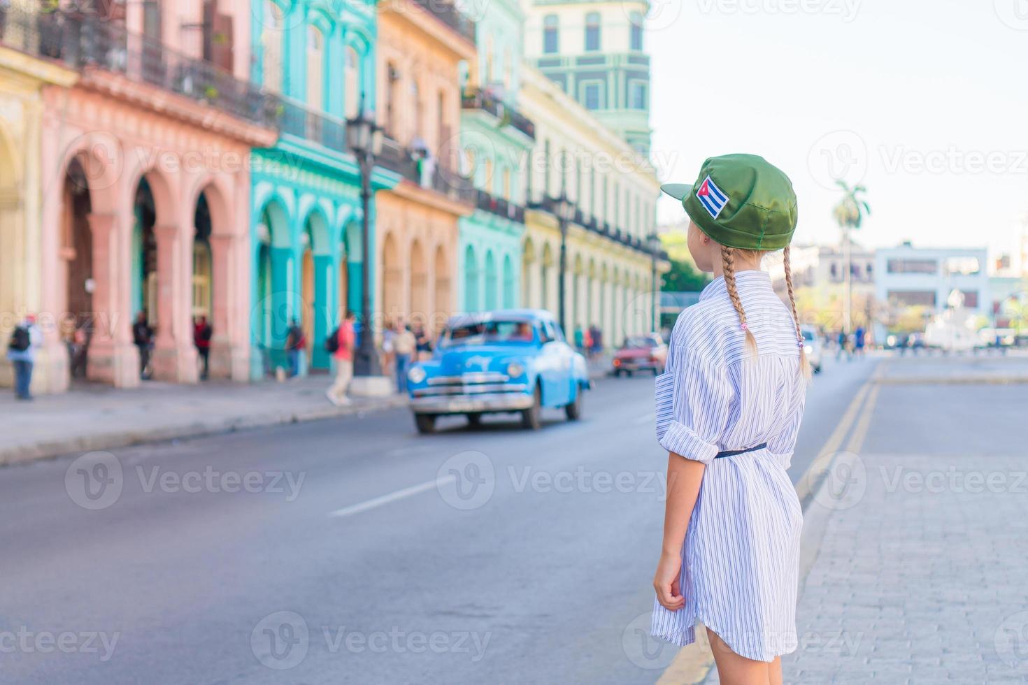 menina na área popular perto de el capitolio na cidade de havana, cuba. retrato de criança fundo clássico carro americano clássico foto