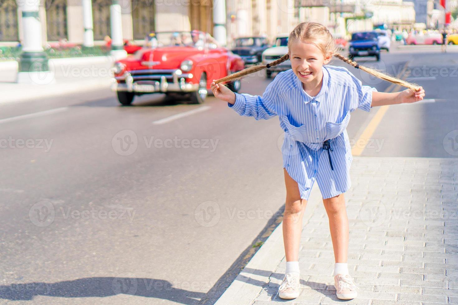 menina adorável na área popular em velha havana, cuba. retrato de criança fundo clássico carro americano clássico foto
