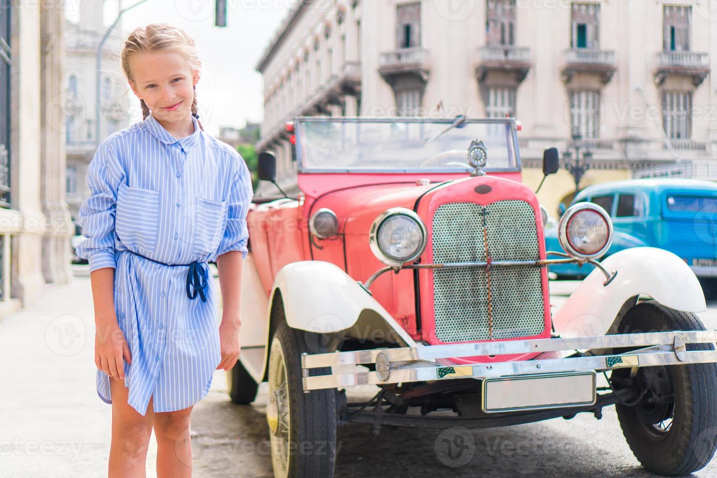 menina adorável na área popular em velha havana, cuba. retrato de criança fundo clássico carro americano clássico foto