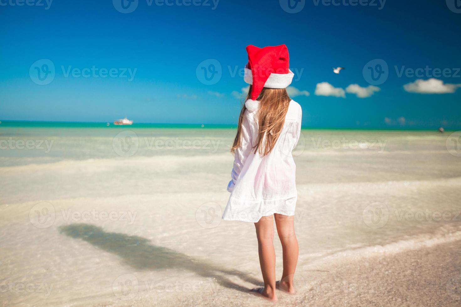 vista traseira da menina bonitinha de chapéu vermelho papai noel na praia foto