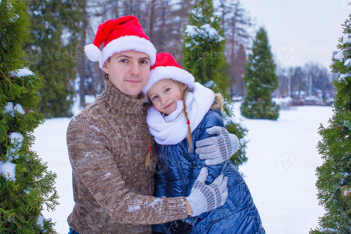 família feliz em chapéus de papai noel com árvore de natal ao ar livre foto