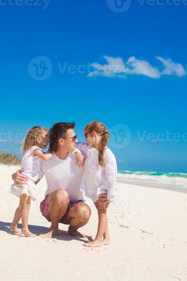 jovem pai feliz e filhas se divertindo na praia branca em dia ensolarado foto