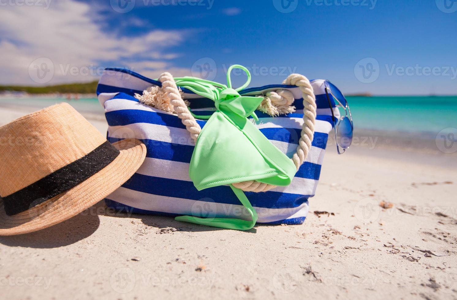 bolsa listrada, chapéu de palha, protetor solar e frisbee na praia tropical de areia branca foto