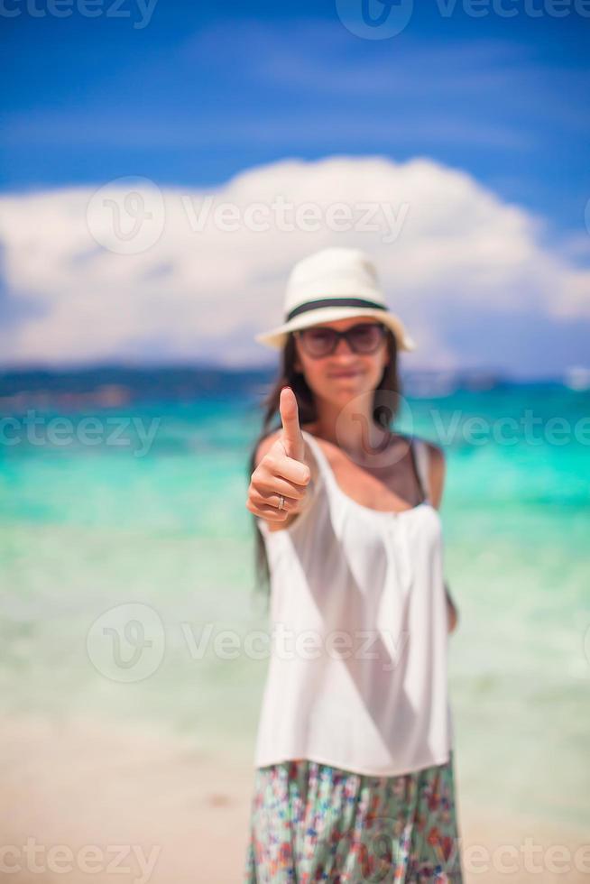 jovem adorável mulher mostrando os polegares para cima na praia branca foto