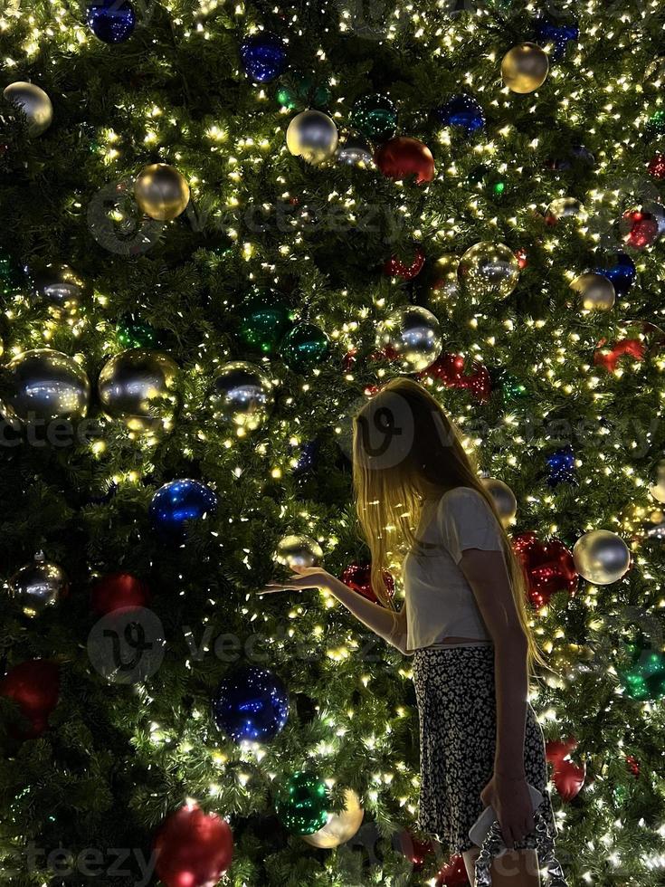 jovem no fundo da árvore de natal em miami. linda árvore de natal na área popular na véspera de natal e luzes foto