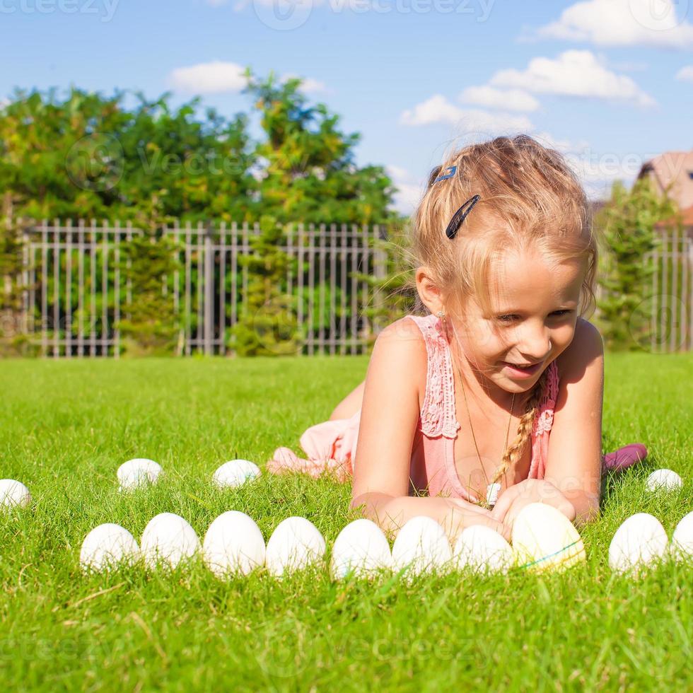 retrato de uma menina feliz brincando com ovos de páscoa brancos na grama verde foto