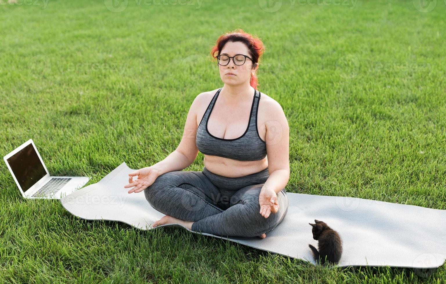 mulher de positividade corporal plus size fazendo meditação no tapete de ioga com gatinho no quintal - conceito de bem-estar e saúde mental foto