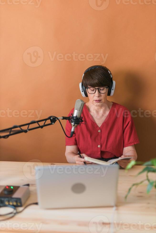 mulher madura fazendo gravação de podcast para seu show online. mulher de negócios atraente usando fones de ouvido na frente do microfone para uma transmissão de rádio foto